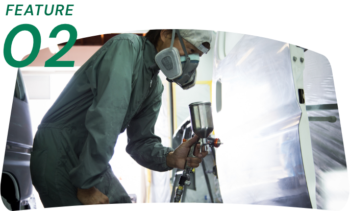FEATURE 02: 防護マスクを着用した作業員がスプレーで車の塗装をしている様子